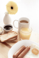 Breakfast with tea, juice, toasts, jam, butter, scrambled eggs, sausages and yellow gerbera flower on wooden table macro  retro style
