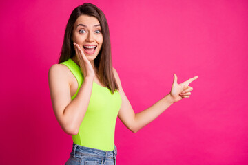 Photo of crazy young lady direct finger empty space open mouth arm cheekbone wear green singlet isolated vibrant pink color background