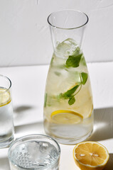 drink, detox and diet concept - glasses with fruit water or lemonade, lemons and peppermint on white table