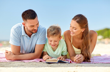 family, leisure and people concept - happy mother, father and son laying and reading book on summer...