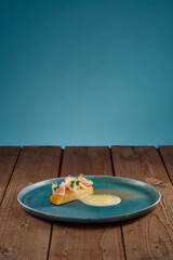Blauer Teller mit gelbem Gemüse und heller Sauce auf Holztisch mit blauem Hintergrund