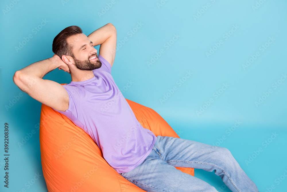 Wall mural photo portrait of bearded hipster chilling during break laying on beanbag smiling isolated on bright