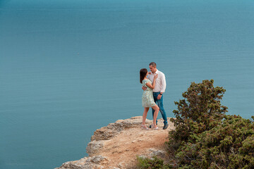 Fototapeta premium Young married couple admires the sea or ocean at edge of a rocky cliff. Family photoshoot on background of crag