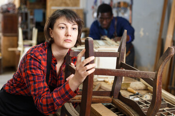 Professional female furniture restorer inspecting vintage armchair in workshop