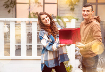 Man giving a Christmas present to his girlfriend. They holding red box with Valentine's gift. Couple smiling and enjoying time together