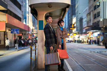 stylish young asian couple standing on street in bus station