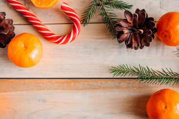 New Year's decor. Christmas tree branches, pine cones, tangerines and candies on wooden background.
