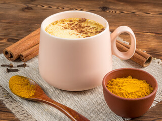 View of a cup of golden milk with turmeric and cinnamon on a wooden background. Soft focus.