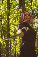 An elven girl with a katana in her hands is walking through the forest and preparing for battle