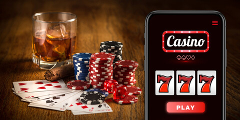 Online gambling, casino concept. Hand holding device with lottery, casino cover. Playing dips and cards on table on the background. Poker, bookmaking, gaming, modern technologies, business and finance