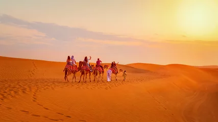 Papier Peint photo Brique Caravan with group of tourists riding camels through Dubai desert during safari adventure