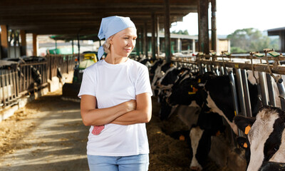 glad senior female farmer posing in cowshed at dairy farm