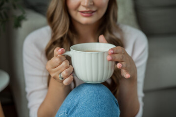 Beautiful young woman drinking hot cocoa and sitting by the window at home
