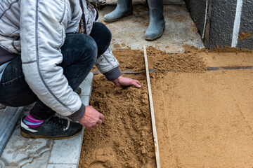 Worker screeding sand bedding to level for laying paving slabs.