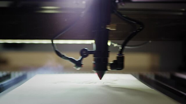Woodburning. Industrial laser is cutting a pattern on a plywood sheet and moving slowly, close up. Modern wood burning with a laser. A red laser beam moves through a tree