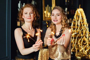 Selective focus. Sparklers in the hands of two beautiful bokeh woman Christmas garlands and gifts. Gold Christmas decoration. Happy New Year.