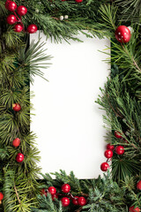 Fototapeta na wymiar Christmas card background. Paper notice sheet with copy space for text. Decorative frame of fir branches and holly berries. Minimal winter or New Year seasonal concept. Flat lay, top view.