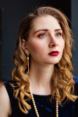 A beautiful women in a blue velvet dress and pearl beads near the window.