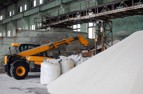 Loader loading jumbo-bags with white urea fertilizer in the warehouse. Selective focus.