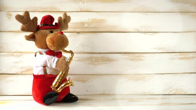 Stuffed reindeer playing saxophone and dancing on a white wooden wall celebrating christmas.