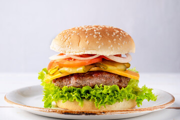 Tasty beef burger with cheese, onion, tomato and lettuce on a plate.