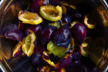 Bunch of ripe purple plums, halved in shiny bowl, freshly washed