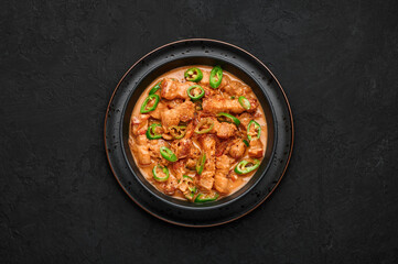 Bicol Express Stew in black bowl on dark slate table top. Filipino cuisine spicy pork belly coconut milk curry. Asian food. Top view