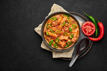 Bicol Express Stew in black bowl on dark slate table top. Filipino cuisine spicy pork belly coconut milk curry. Asian food. Copy space. Top view