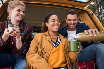 Friends sitting at their car and drinking hot beverage
