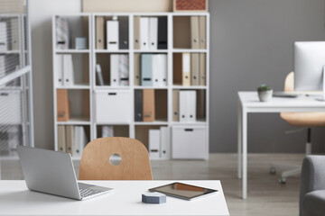 Image of empty workplace with laptop and bookcase in the background at modern office