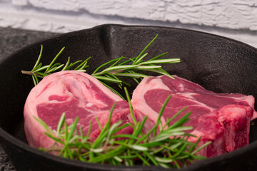 Lamb loin chops with rosemary in a cast iron frying pan.  On a black granite and grey brick background - obrazy, fototapety, plakaty