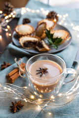 masala tea and sweet mince pies on a table with Christmas decoration. Masala chai is an Indian tea beverage made by boiling black tea in milk and water with a mixture of aromatic herbs and spices