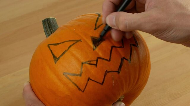 A man carves out a festive Halloween decor with his own hands. Scary pumpkin for Halloween in preparation. Drawing and carving pumpkin close-up.