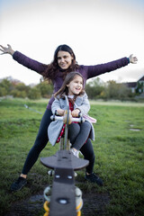 Joyful mother and little daughter smiling while playing on a seesaw