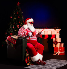 Photo of santa sit chair hold mug telephone look screen wear x-mas suspenders cap isolated decorated background