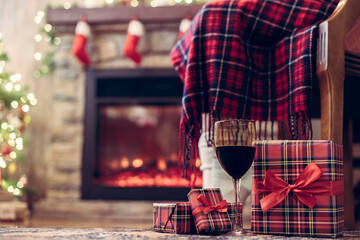 Legs of disabled woman in a socks covered plaid sitting and relaxation on armchair near fareplace and christmas tree with glass of wine after finishing pakking gift boxes for family. Bottom view.