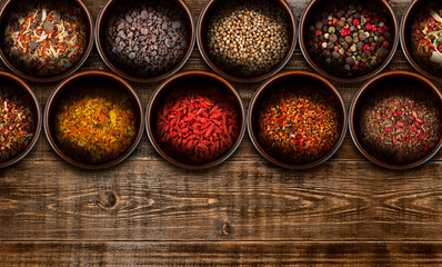 Obraz na płótnie Canvas Texture of various spices on a wooden table. Seasonings and spices in brown clay bowls on an old shabby board. Multicolored spices for cooking.