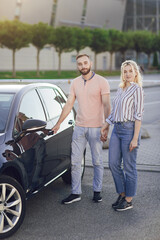 Man giving surprise to woman by purchasing a new car. Young couple, man and woman, buy a car outdoors. Buying a new car from the salon. Test drive a new car