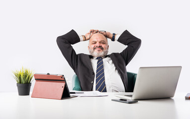 Mature Asian Indian businessman relaxing or resting in armchair with legs up on office desk