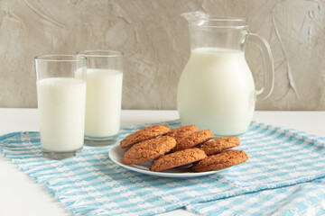 a carafe of cool milk with oatmeal cookies - the taste of childhood. concrete background, blue checkered napkin