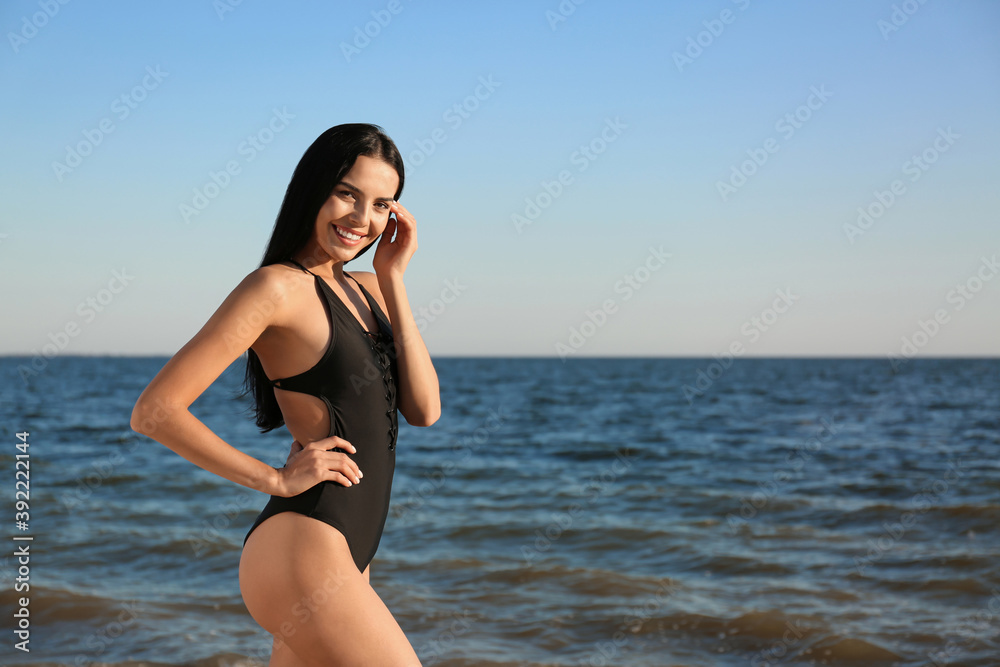 Sticker beautiful young woman in black stylish swimsuit on beach. space for text