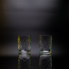 Two crystal glasses on a black background. Decorated with carvings, ornaments. On the edges there are multi-colored highlights. Reflection.