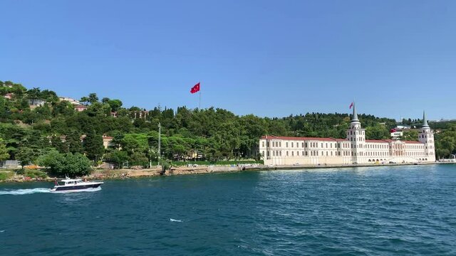 Footage of yacht passing in Kandilli / Cengelkoy area of Istanbul on Bosphorus strait. Kuleli military school is in the view. Beautiful scene. It is a sunny summer day. Camera moves forward.