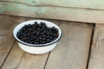Freshly picked blackcurrants in a white bowl on a wooden background.