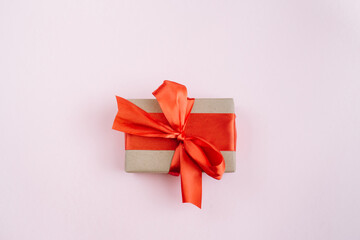  Present box with red bow on pastel pink background. Flat lay, top view, copy space.