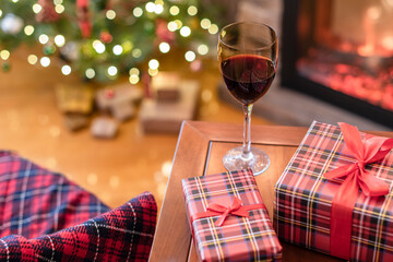 Armchair with plaid, packing gift boxes for family and glass of wine near christmas tree and fireplace. Top view