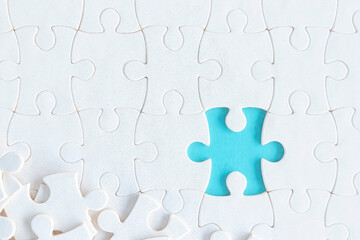 Assembling jigsaw puzzle pieces, Top view unfinished white jigsaw puzzle on blue background, Fragment of a folded white jigsaw puzzle with copy space, Teamwork and problem solving concept.