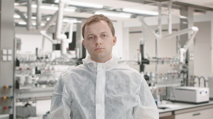 Fototapeta premium Caucasian male scientist wearing protective suit and mask posing in a laboratory, crossing hands and looking into camera