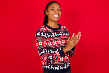Young beautiful African American woman standing against red background clapping and applauding happy and joyful, smiling proud hands together.