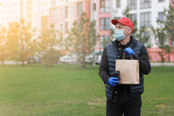 Delivery man in red cap, face medical mask, gloves hold take away paper bag and drink in disposable cup outdoors in city. Service coronavirus. Online shopping